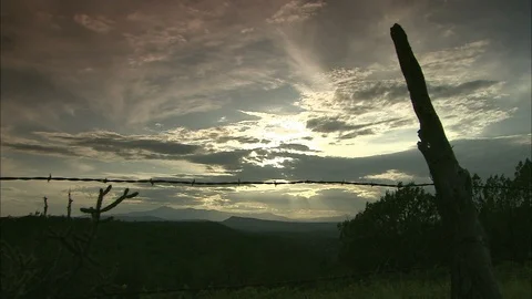 Sunset with sun breaking through clouds and post with barbed wire in foreground Video stock 95601455