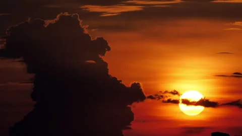 Sunset sun disk descending beside towering silhouetted cumulus cloud, time-lapse Stock Footage 346162389