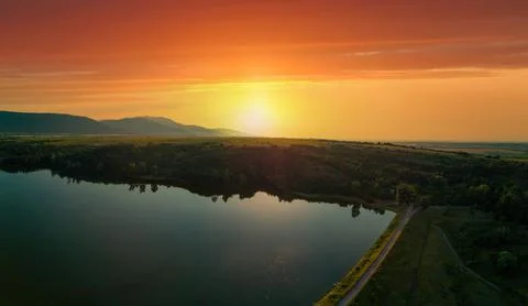 Sunset sun illuminates fields, silhouettes of Balkan mountains and lake Фото