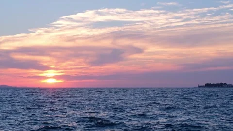 The sunset sun sets in beautiful patterned clouds over a dark blue sea with Stock Footage 285741058