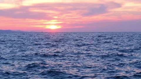 The sunset sun sets in beautiful patterned clouds over a dark blue sea with Stock Footage 285741621