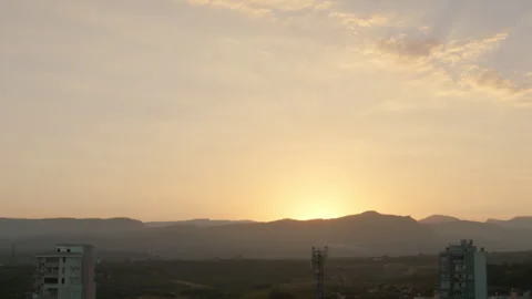 Sunset, the sun sets down behind the mountain, sun rays in the haze, cityscape Stock Footage 303630833