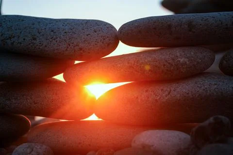 Sunset sun shining through stacked stones on the shore Stock Photos