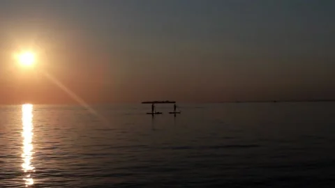 At Sunset Sup Serfers Float Sail Past An Island In The Ocean Stock Footage 168173967