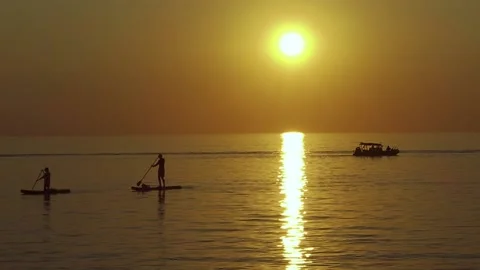 At Sunset Sup Serfers Float Sail Past A Fishing Boat In The Sea Stock Footage 168173973