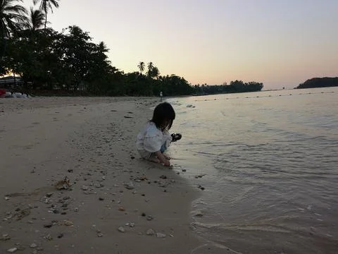 Sunset Thai beach,  coconut trees.  A little girl picks up shells on the beach. Stock Photos