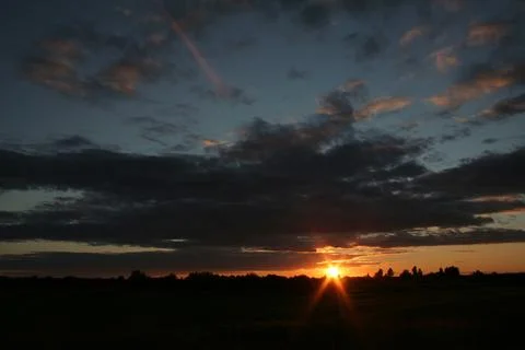 "Sunset Through Clouds Over a Darkened Landscape" Stock Photos
