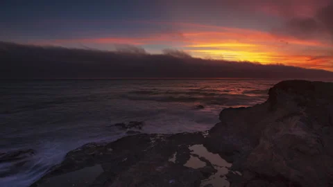 Sunset through gray clouds over coastal rocks - timelapse Stock Footage 220528691