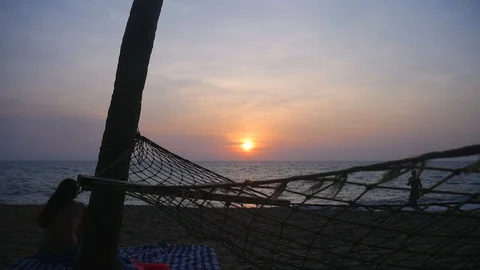 Sunset through hammock and man swimming at the sunset Stock Footage