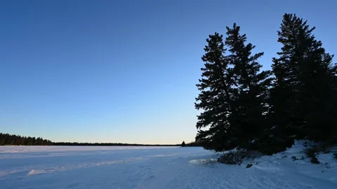 Sunset time lapse with clear sky over a large snow-covered lake with pines trees Stock Footage 146334448
