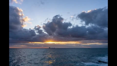 Sunset timelapse of passing clouds and moving sea with ship on the background Video stock 292561106