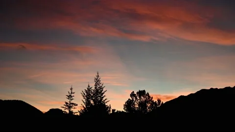Sunset timelapse with trees and mountains in the foreground.  Stock Footage 219225131