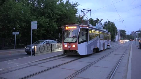 Sunset tram with electric lighting passes tracks crossing towards city center Stock Footage 64638799