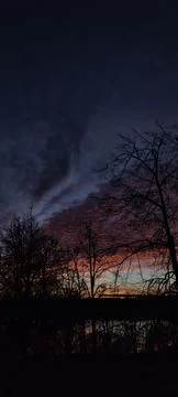 A sunset with trees in front and a dark sky behind Stock Photos