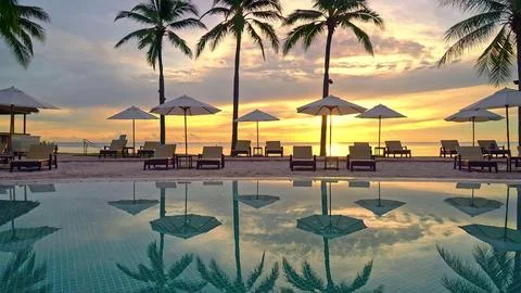 Sunset view of a beach with palm trees and lounge chairs Stock Photos
