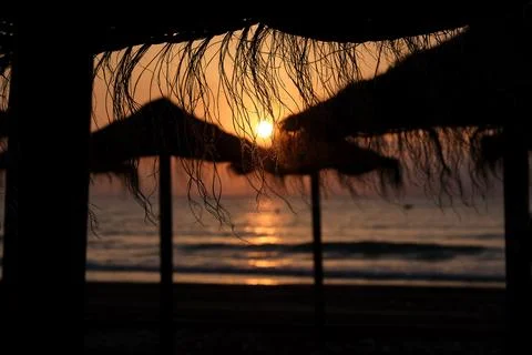 Sunset view behind beach umbrellas at coastal location during evening hours Foto stock