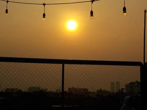 Sunset view behind a chain-link fence stands, adorned with string bulb lights. Stock Photos