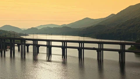 Sunset view of a bridge over a river with mountains in the background at a quiet Stock Footage 344793909