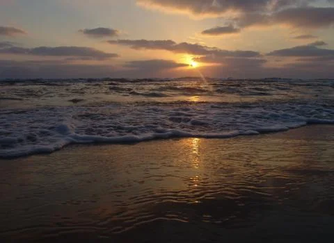 Sunset view on a calm sandy beach with cloudy sky and golden light. 写真素材