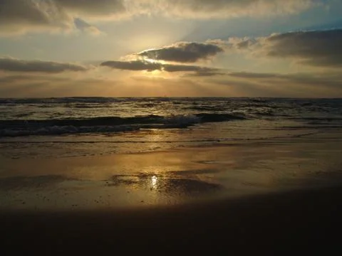 Sunset view on a calm sandy beach with cloudy sky and golden light. 写真素材