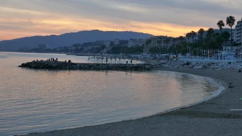 Sunset view of Cannes beach with silhouettes of people on rocks, palm trees Stock Footage 318194911