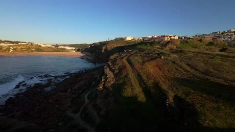 Sunset view of coastal cliffs with crashing waves and distant town Video stock 344563186