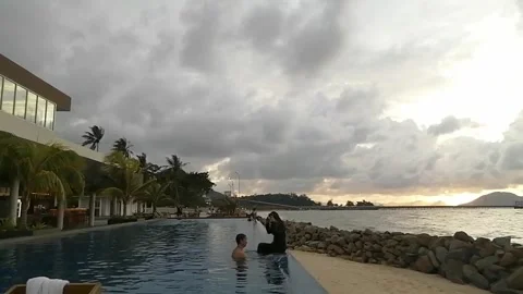 Sunset view with a couple in the pool facing the ocean Stock Footage 268130771