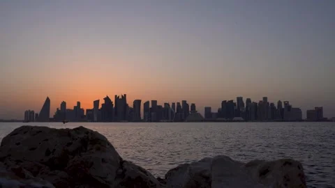Sunset View of Doha Skyline from Rocky Shoreline Stock Footage 336565735