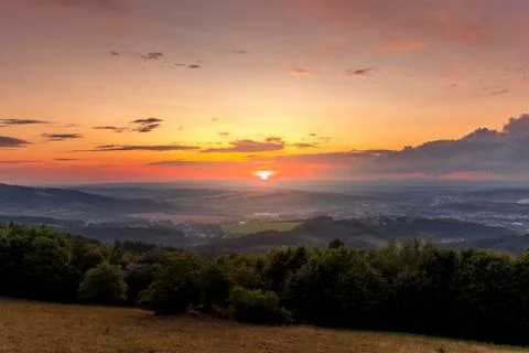 Sunset with view on landscape with fully colored clouds and orange sun goes d 库存照片