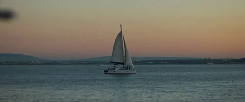 Sunset view of a lonely boat sailing in the ocean, with a city harbor in the  Stock Footage 147568261