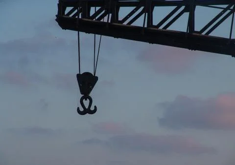 Sunset view of a metal double hook hanging with ropes from a tall crane 写真素材