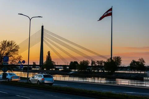 Sunset view of a modern cable-stayed bridge with a large flag, parked cars .. Stock Photos