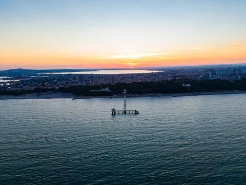 Sunset view over the coastline with a lighthouse in the sea and a city skyl.. Stock Photos