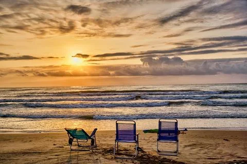 Sunset view over the ocean with beach chairs set on the sand near the water.. Stock Photos
