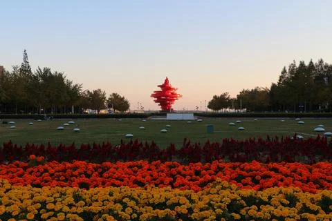 Sunset view of red sculpture surrounded by vibrant flowers in public park Foto stock