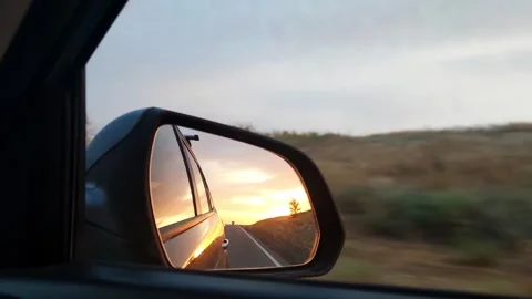 Sunset view in the side view mirror of a car driving on the road in the field Stock Footage 243821002