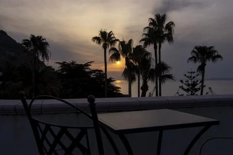 Sunset view through palm trees from balcony with table and chairs Stock Photos