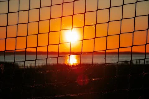 Sunset view through a wire mesh fence, with vibrant orange and yellow hues .. Stock Photos