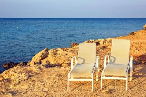 Sunset view to two parallel sunchairs placed near water 库存照片