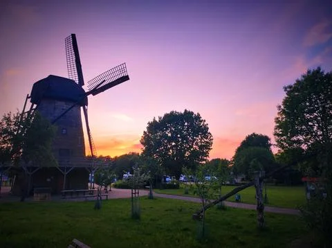 Sunset view of a windmill and trees in a park during evening hours in a rur.. Stock Photos