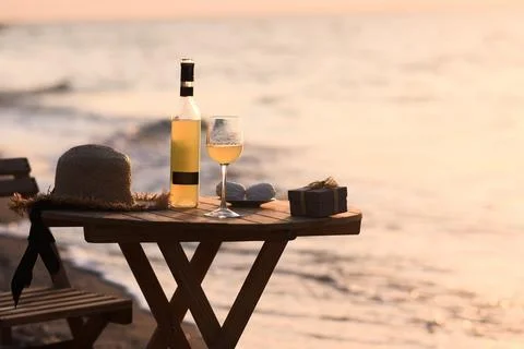 Sunset view with wine bottle and glass on wooden table beside sea. Stock Photos