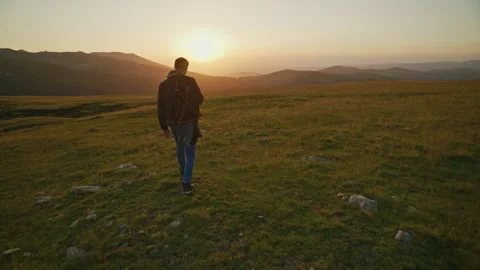 Sunset walk on a mountain trail with a person heading towards a distant horizon Stock Footage 345640367