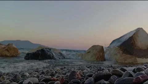 Sunset Wave Splash Through Coastal Boulders on a Pebble Beach Stock Footage 338185350