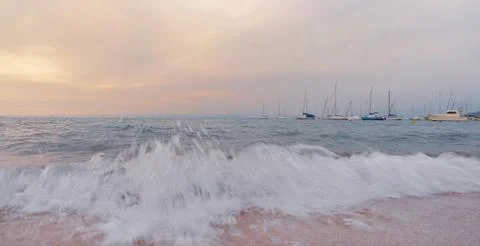 At sunset the waves break on the beach in front of boats Stock Photos