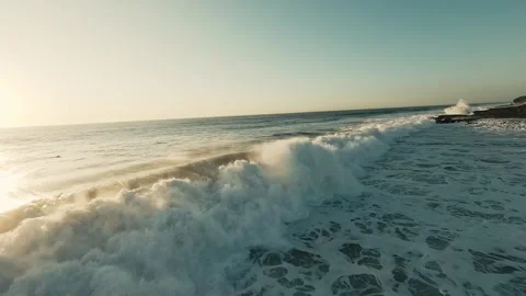 Sunset waves crash against rocky shore with foam Stock Footage 339785975