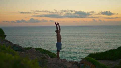 Sunset yogi silhouette training standing head at ocean cliff. Fit man practicing Stock Photos