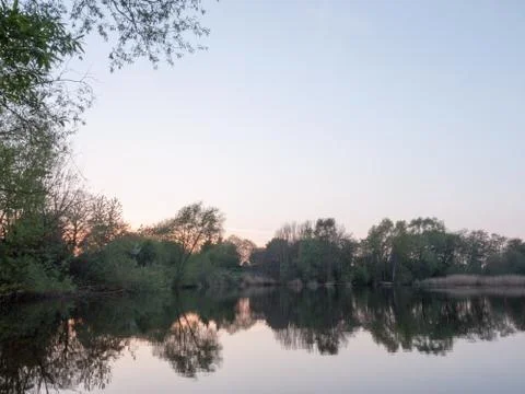 Sunsetting over a lake as the trees around are reflected in the water Stock Photos