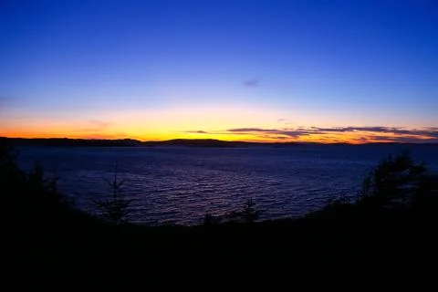 Sunsetting over the ocean with silhouette of the trees Stock Photos