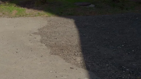 Sunshine illuminates gritty asphalt with cracks and scattered stones vividly Video stock 333908266
