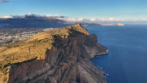 Sunshine illuminates steep cliffs and deep waters with distant island views.. Stockfoto's